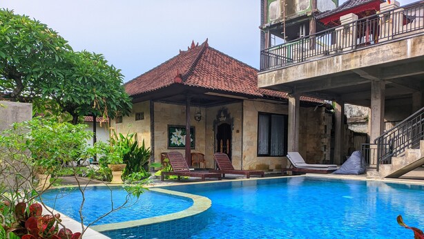 Piscina com espreguiçadeiras, área de estar coberta e escada para uma varanda.