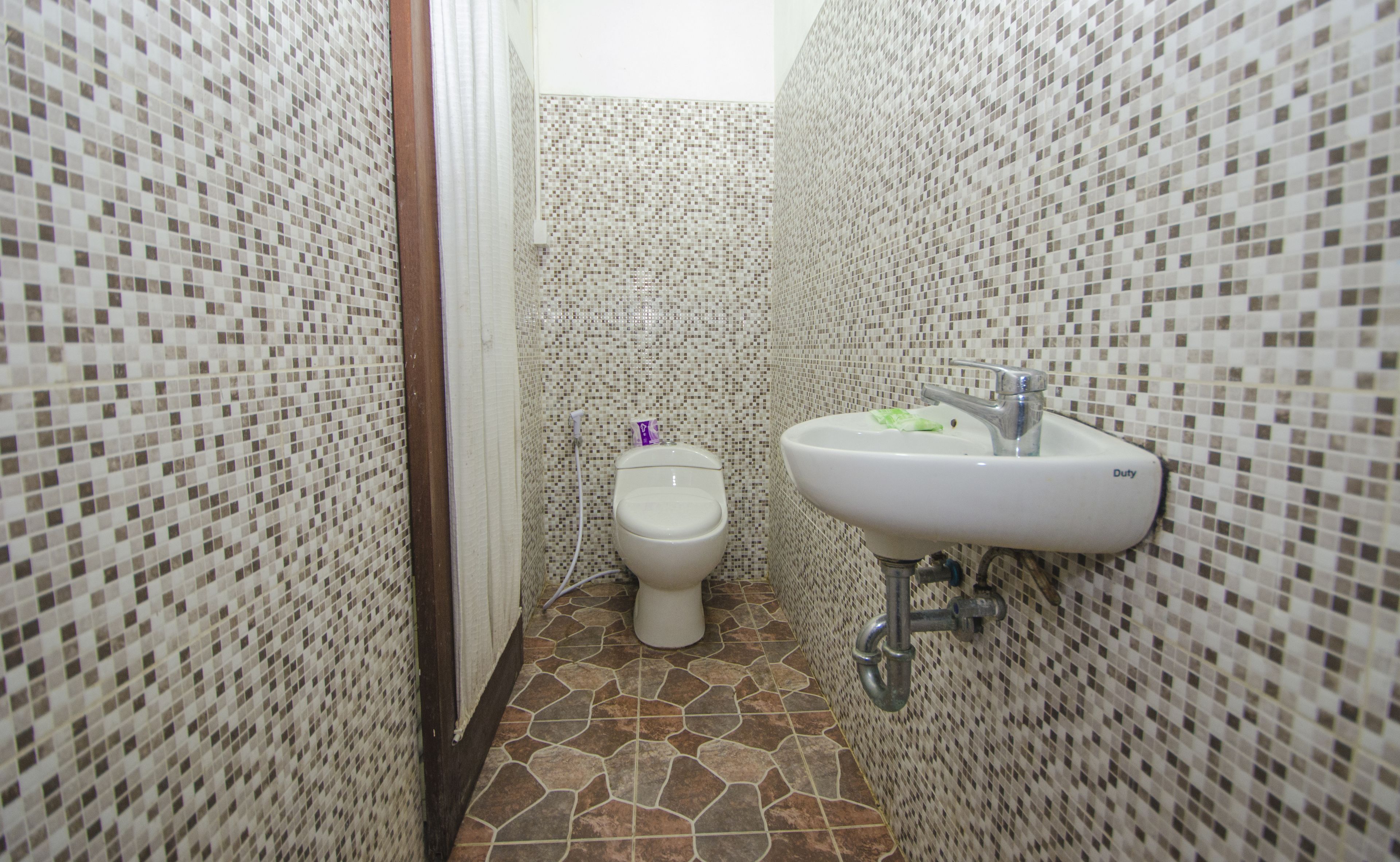 A bathroom with mosaic tiled walls, a toilet, and a sink with a faucet.