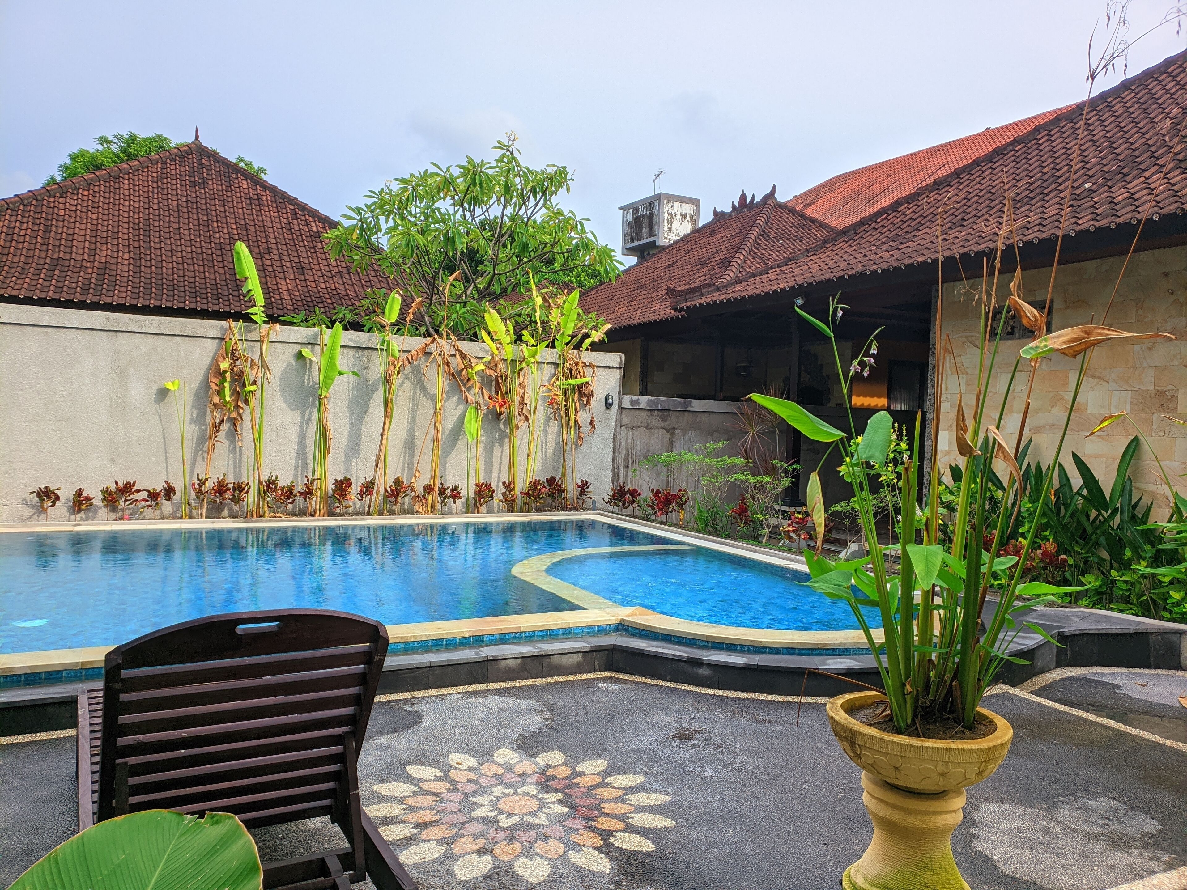 A swimming pool with a tiled edge, surrounded by potted plants and a chair.