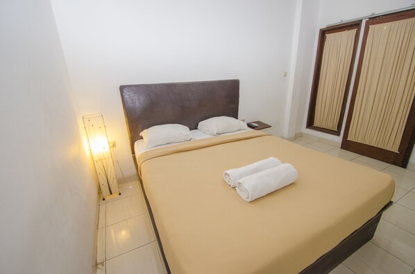Una cama bien hecha con un cabecero marrón, almohadas blancas y una toalla blanca enrollada.