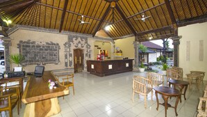 Um hall amplo com teto alto, balcão de recepção e várias mesas e cadeiras de madeira.