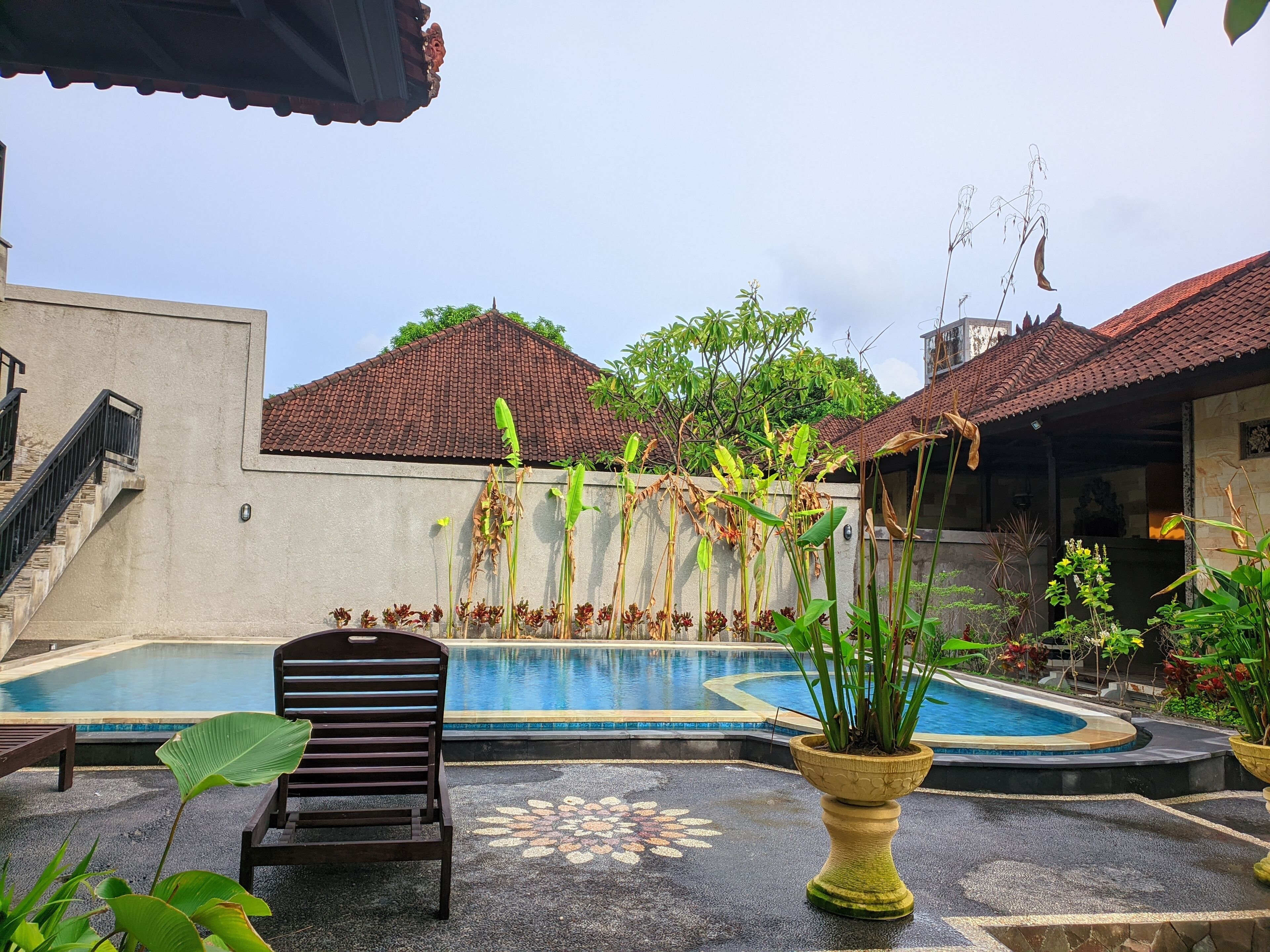 Piscina com deck revestido, uma cadeira e um vaso de planta.