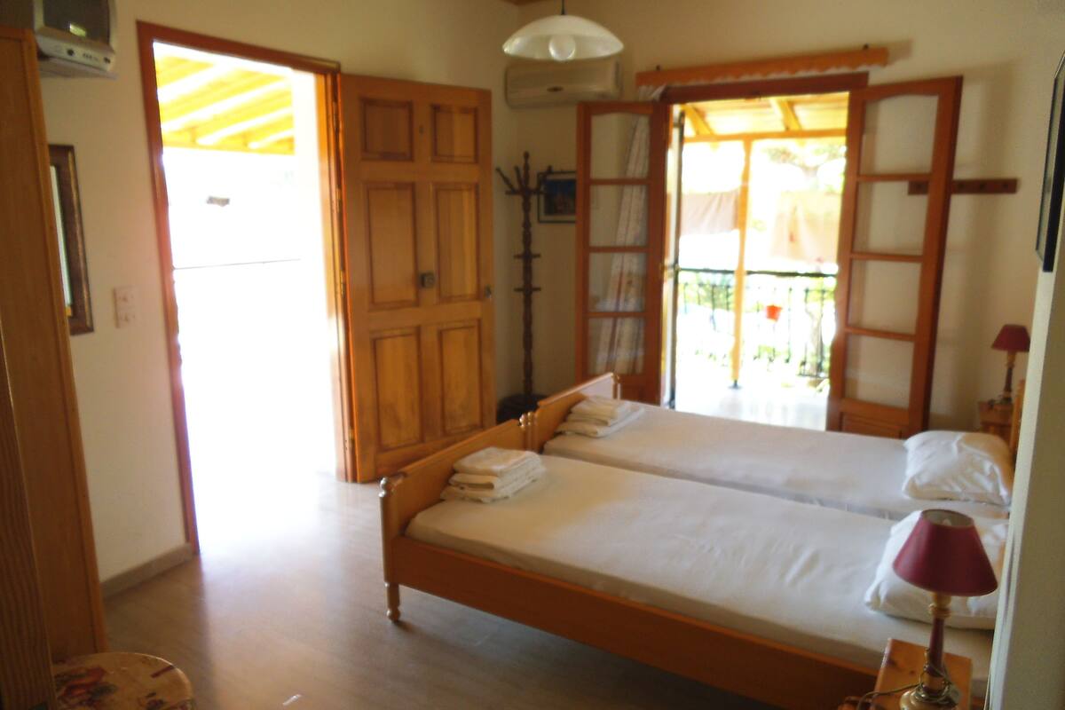 A double bed with a wooden frame, a bedside lamp, and a window with a view of the outdoors.