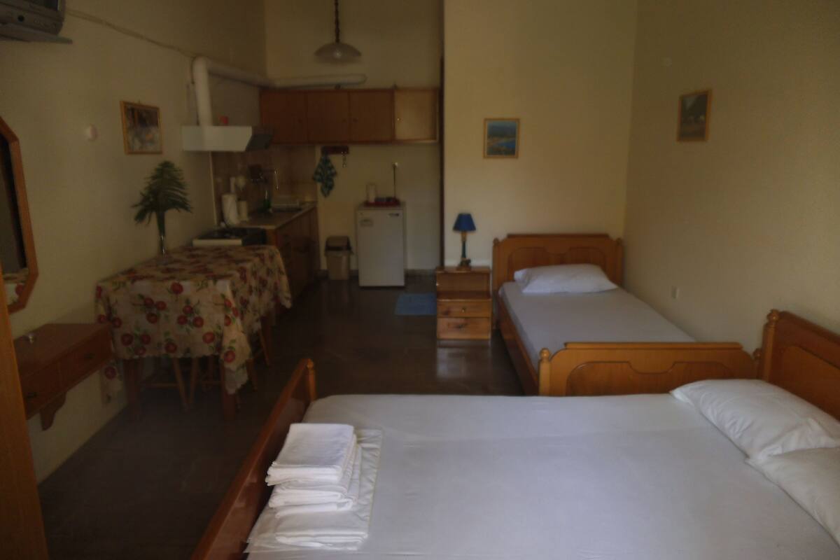 A hotel room with two single beds, a small kitchenette, a dining table, and a mirror.