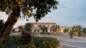 Un edificio moderno con fachada de piedra, rodeado de un jardín ajardinado con plantas florecientes y un árbol grande.