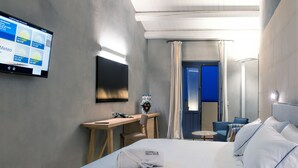 Habitación de hotel con cama, escritorio, silla, televisor en la pared y baño visible a través de una puerta.