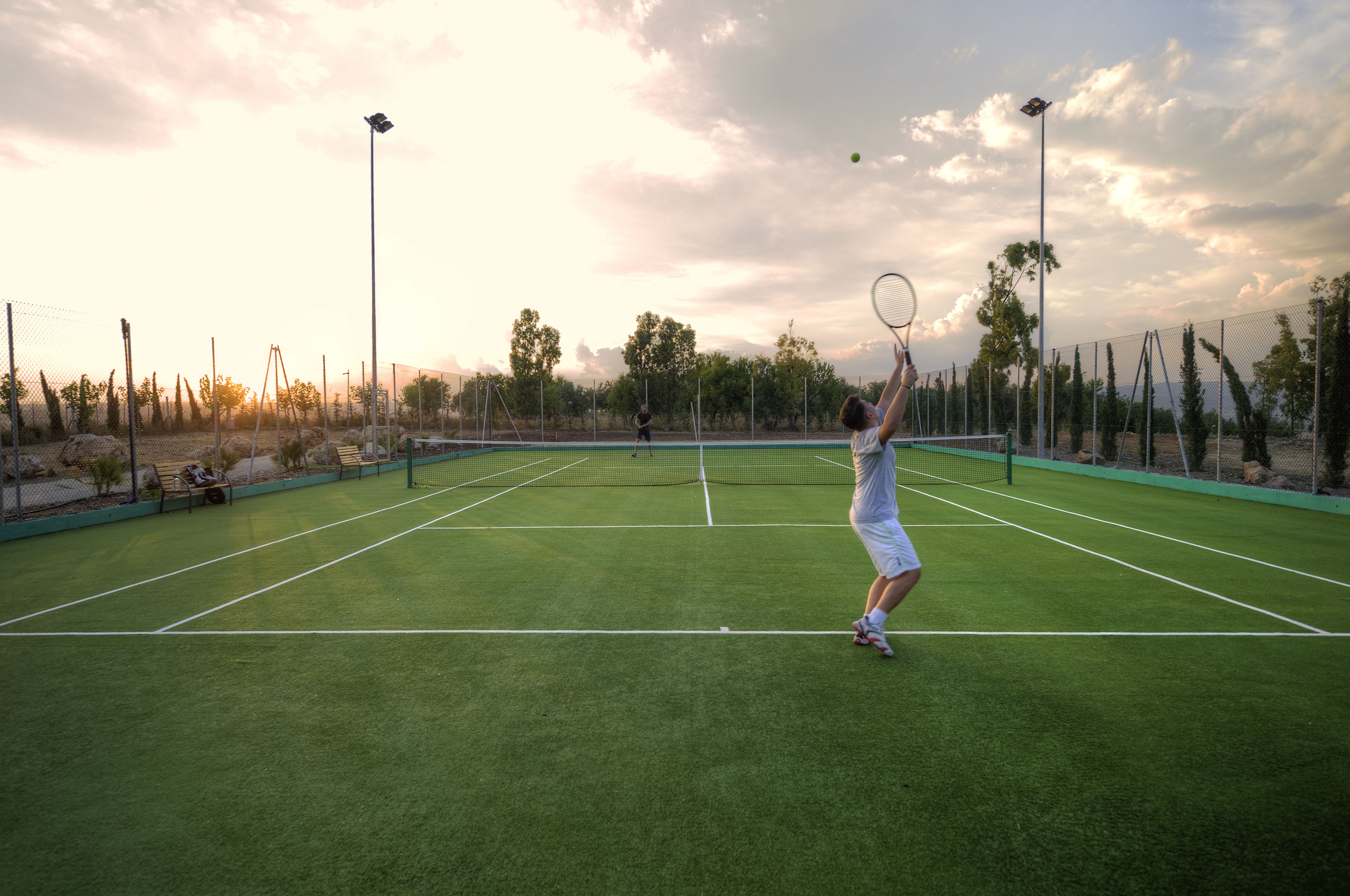 A tennis court with a net, surrounded by a fence, and trees in the background.