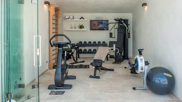 Uma academia em casa com equipamentos de ginástica, uma TV e uma prateleira fixada na parede com objetos.