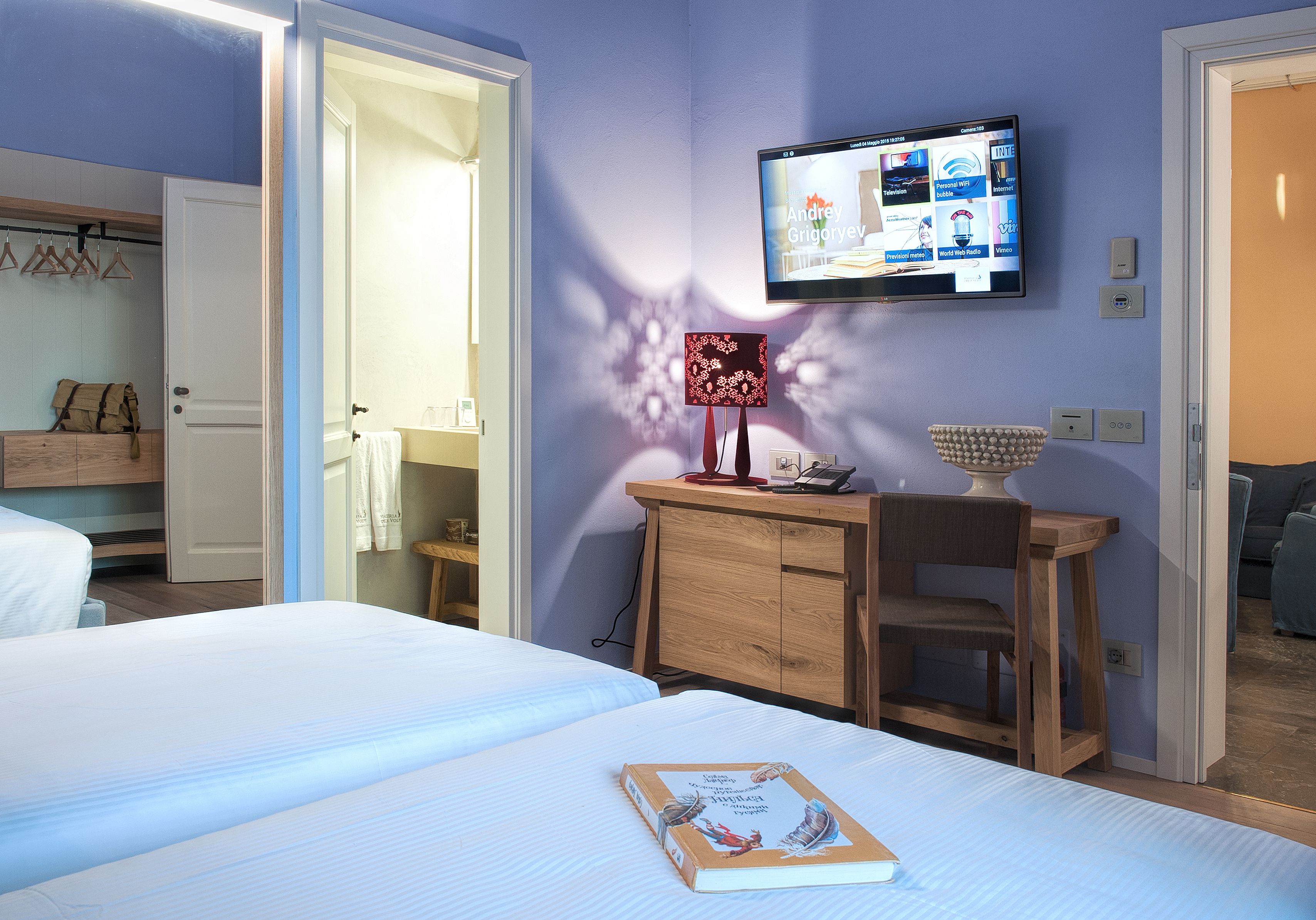 Une chambre d’hôtel avec un lit, un bureau doté d’une lampe, un téléviseur fixé au mur et une salle de bain visible à travers une porte ouverte.