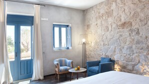 Un dormitorio con pared de piedra, una cama, una silla, una mesa con fruta y una lámpara.