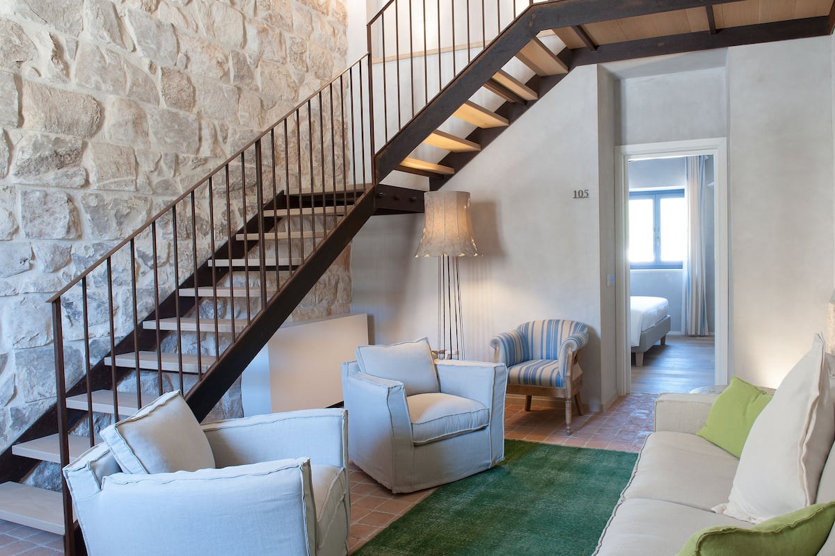 A staircase with a stone wall, a white sofa, a green rug, and a striped chair.