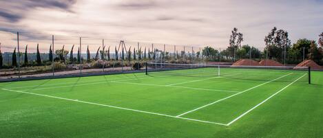 A tennis court with a net, surrounded by a fence and trees.