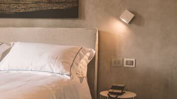 Un letto rifatto con lenzuola bianche e un cuscino, un tavolino rotondo con un laptop e un telecomando, e un lampadario fissato alla parete.