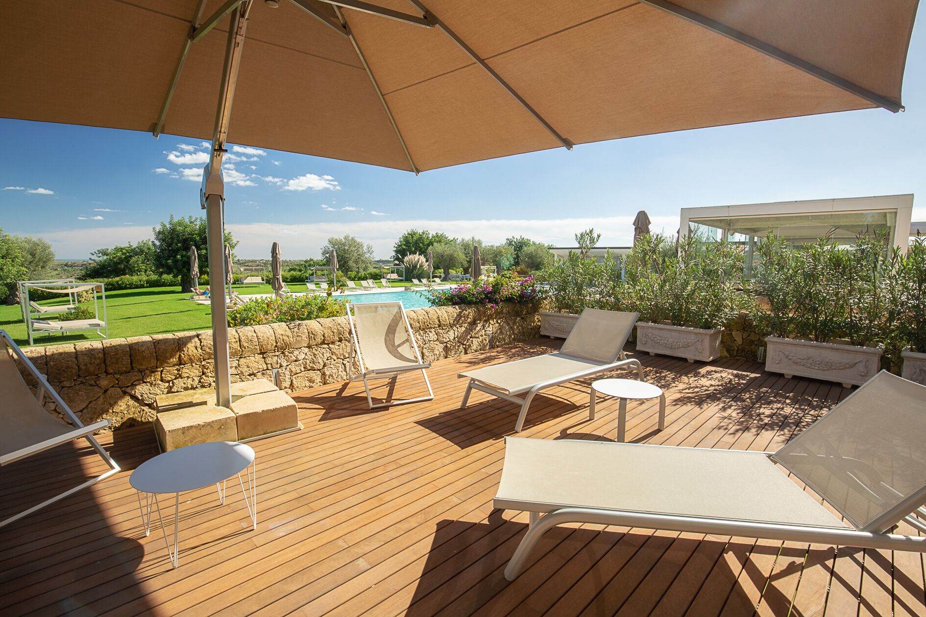 Une terrasse en bois avec des chaises longues et une table, donnant sur une piscine et un espace verdoyant.