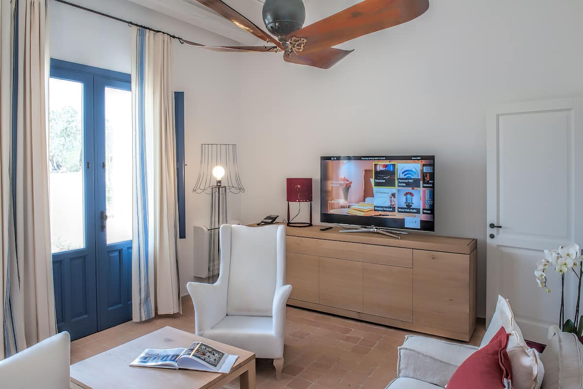 A room with a television, a desk, a chair, a cabinet, and a ceiling fan.
