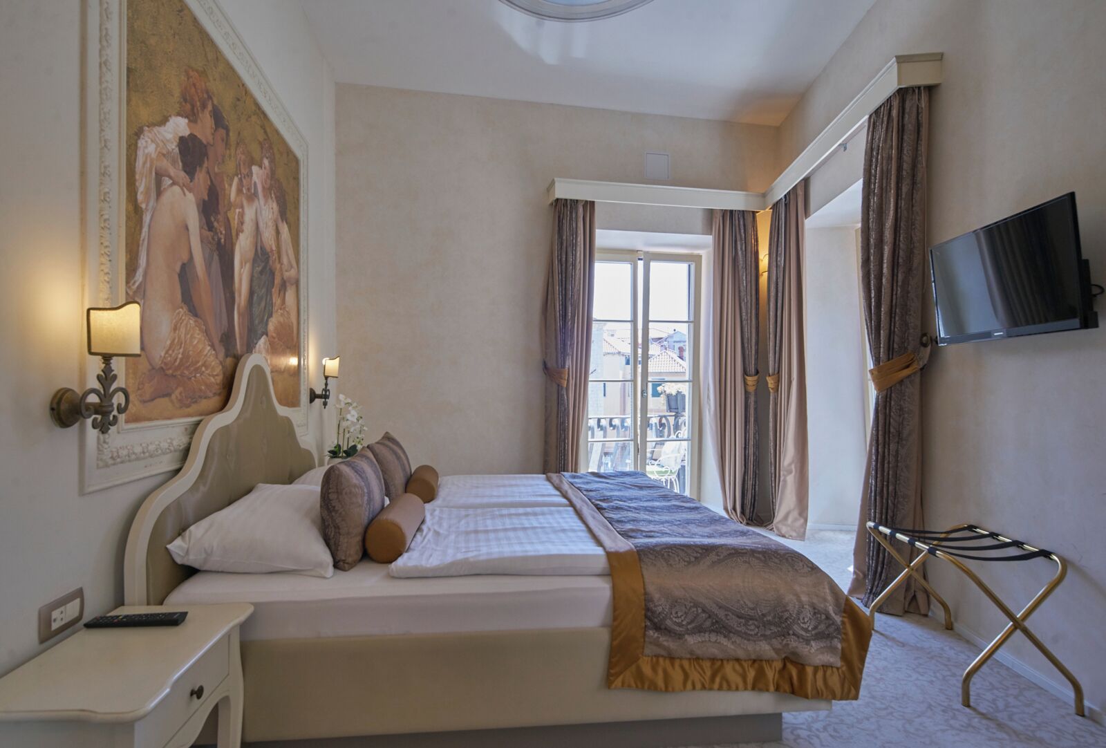 Ein Hotelzimmer mit einem großen Bett, einem an der Wand montierten Fernseher und einem Gemälde über dem Bett.