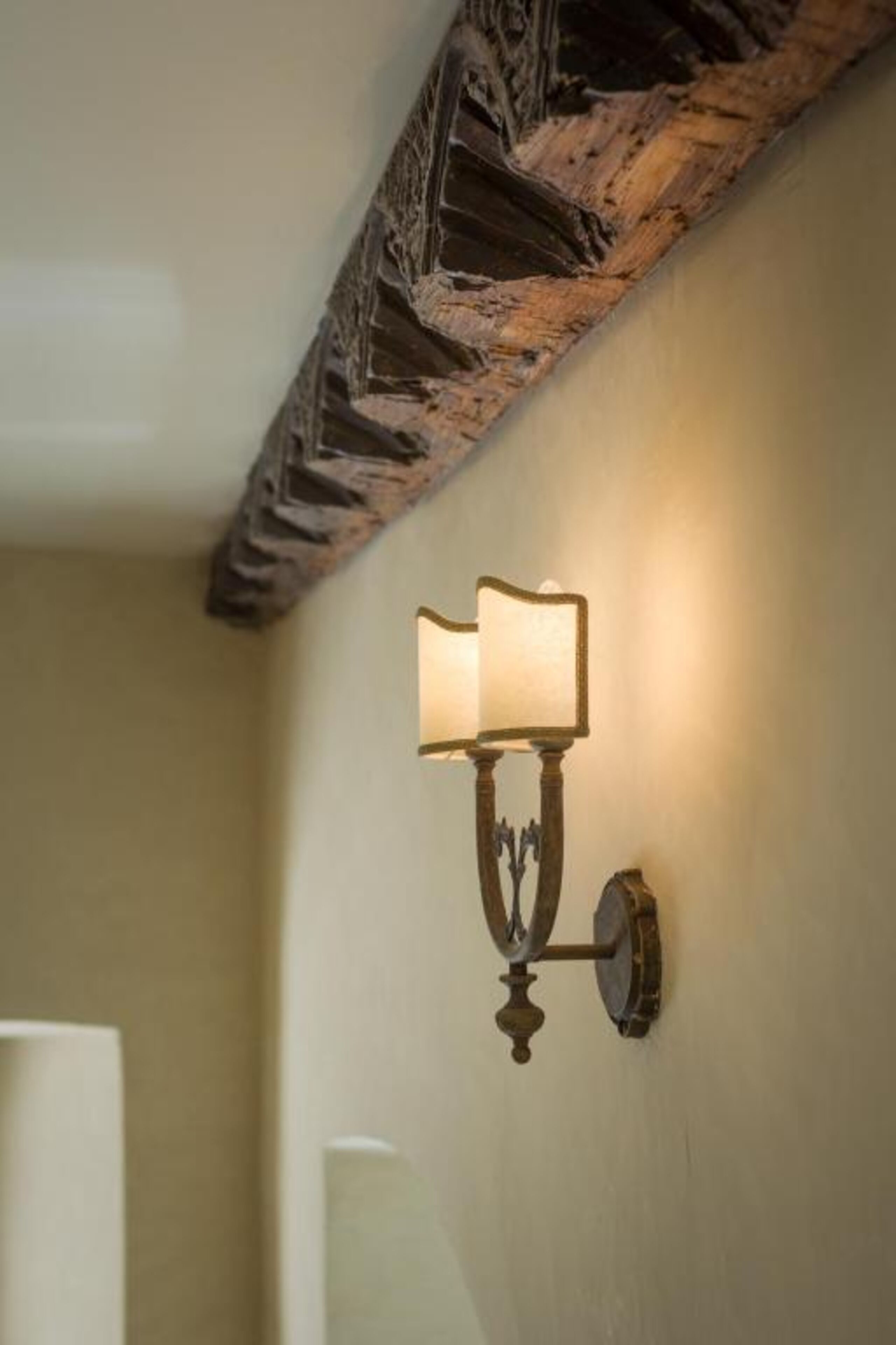 A wall-mounted light fixture with a classic design, a wooden ceiling beam, and a plain wall.