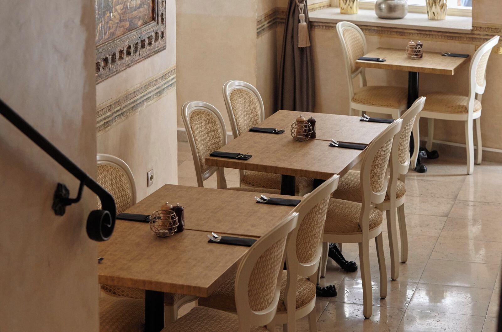 Comedor con mesas de madera y sillas de mimbre, una ventana con vistas y un adorno en la pared.