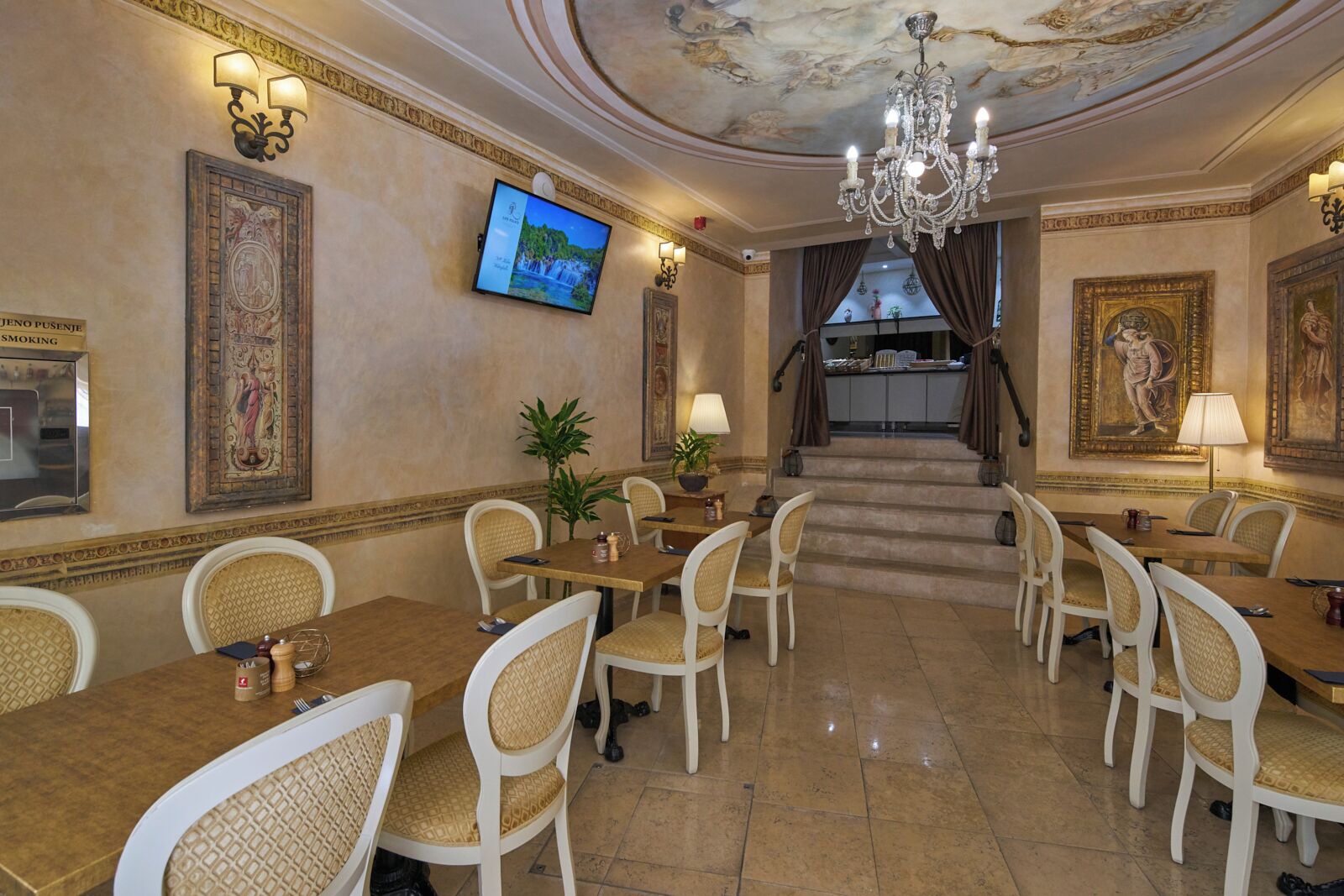 A dining area with multiple tables and chairs, a television mounted on the wall, and a staircase leading to an upper level.