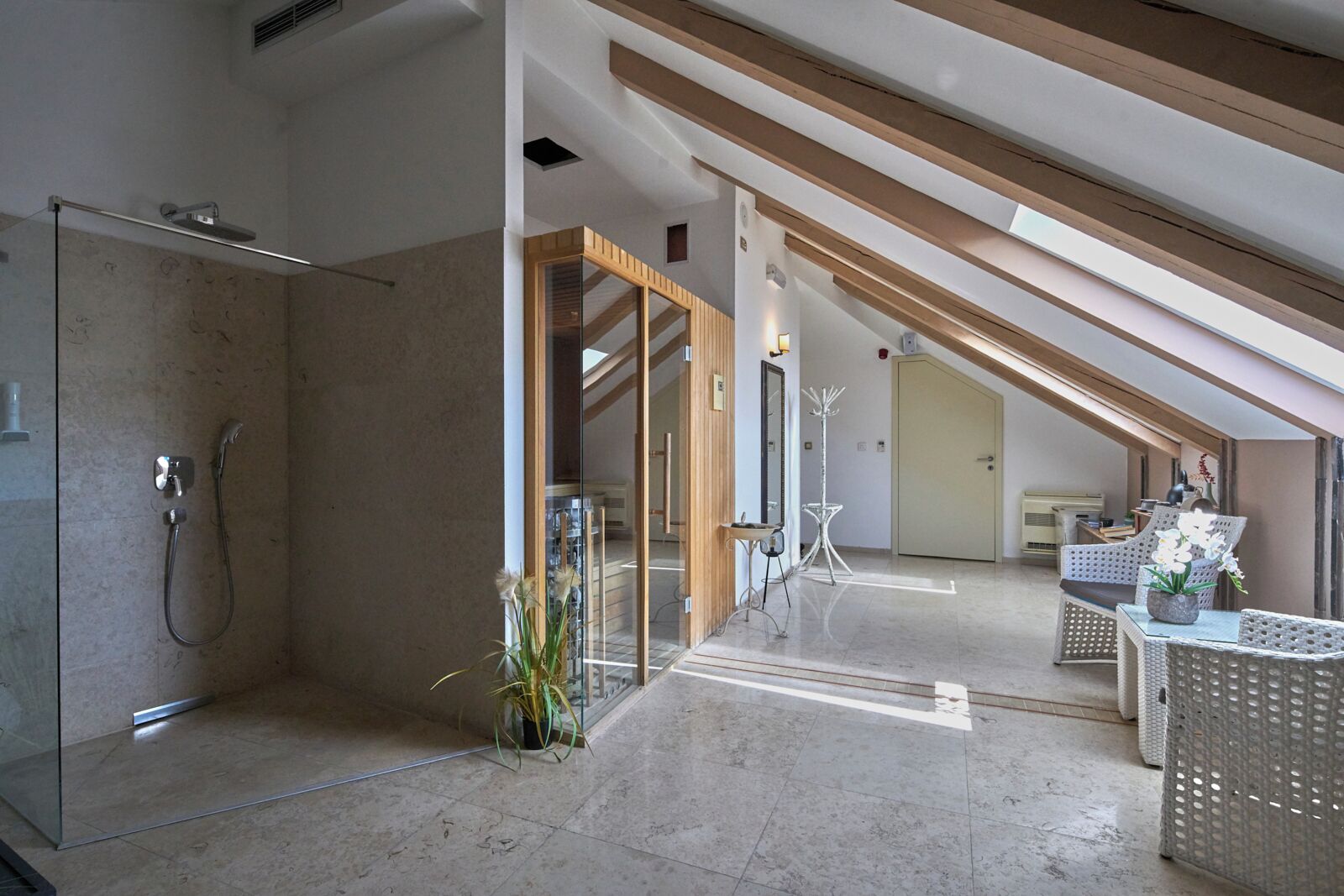 A modern bathroom with a glass shower enclosure, a potted plant, and a wooden ceiling beam.