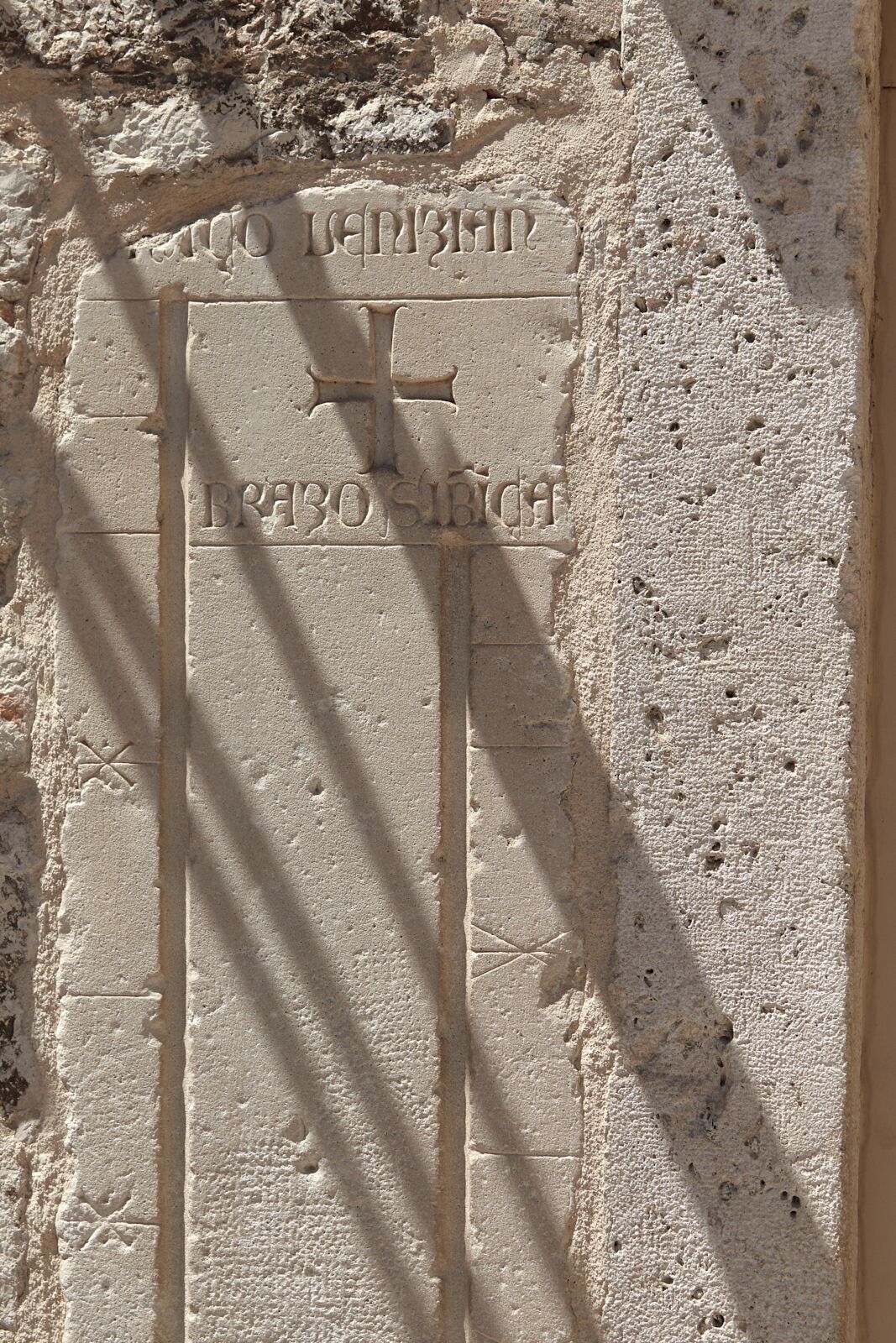 A stone wall with carved inscriptions and a cross symbol.