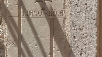 A stone wall with carved inscriptions and a cross symbol.