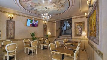 A dining area with a chandelier, a television, and classical paintings.