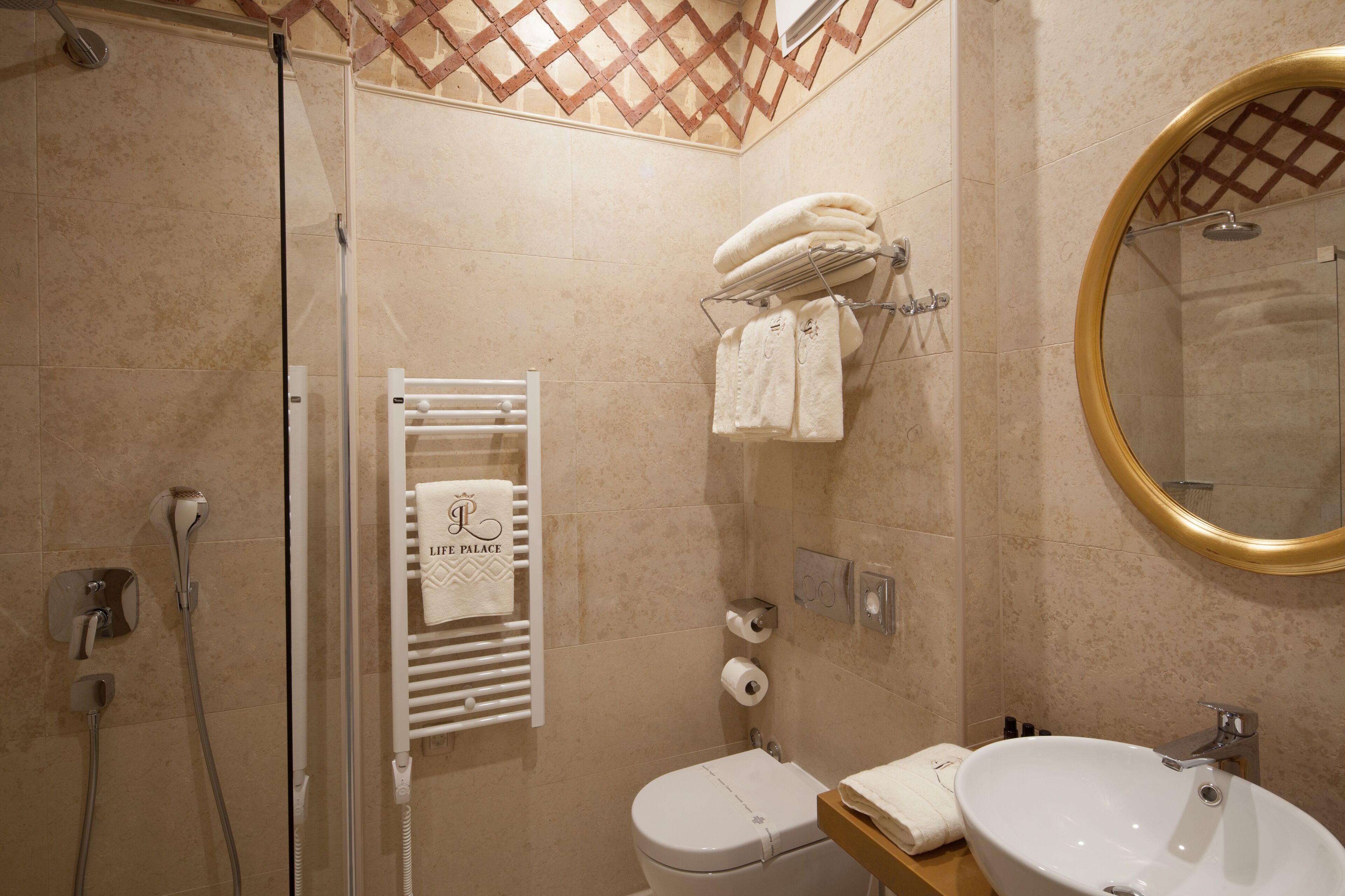 A bathroom with a glass-enclosed shower, a white toilet, a sink with a mirror, and a towel rack with multiple towels.