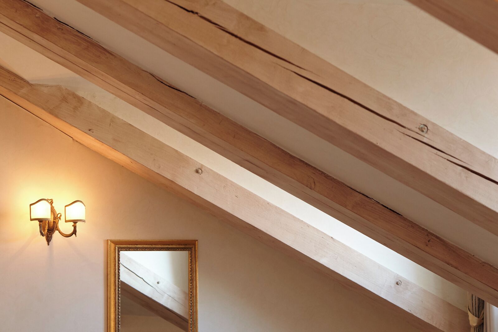 A room with exposed wooden beams, a wall-mounted light fixture, and a mirror.