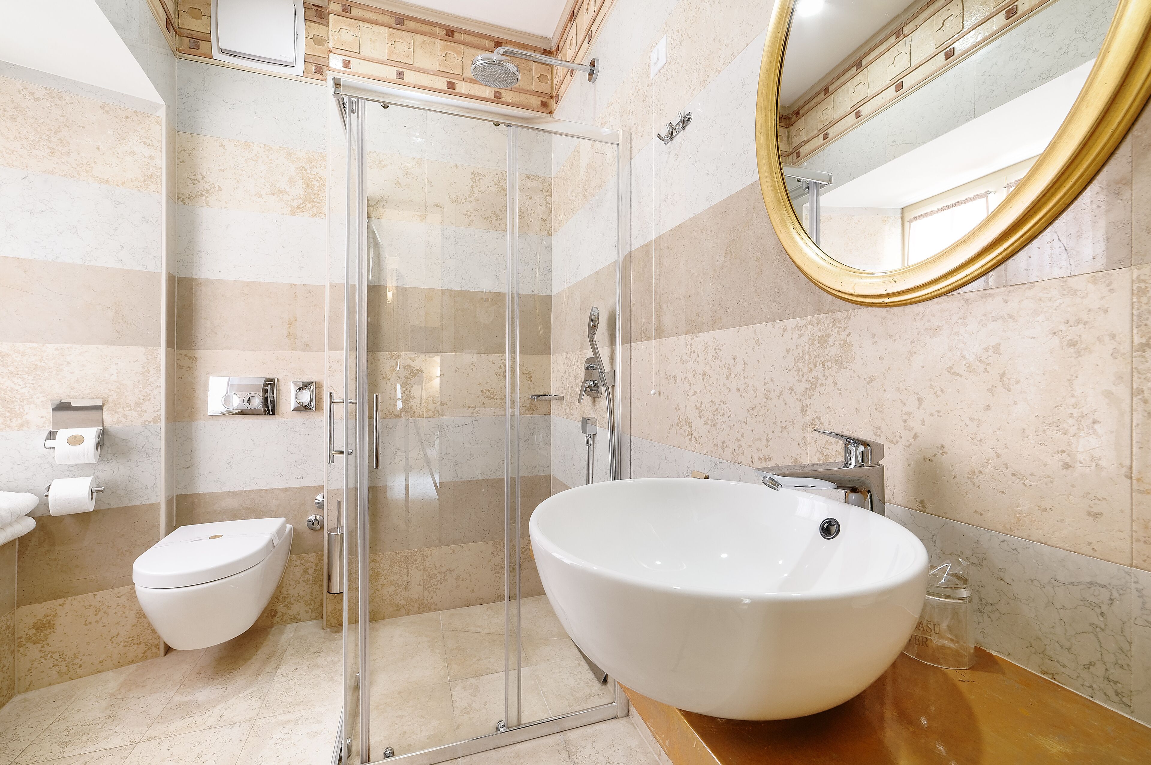 A modern bathroom with a glass-enclosed shower, a white sink, and a marble-tiled wall.
