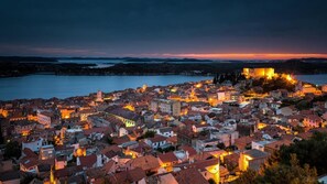 A coastal town at dusk with illuminated buildings and a prominent castle on a hill. - Heritage Hotel Life Palace (Sibenik)