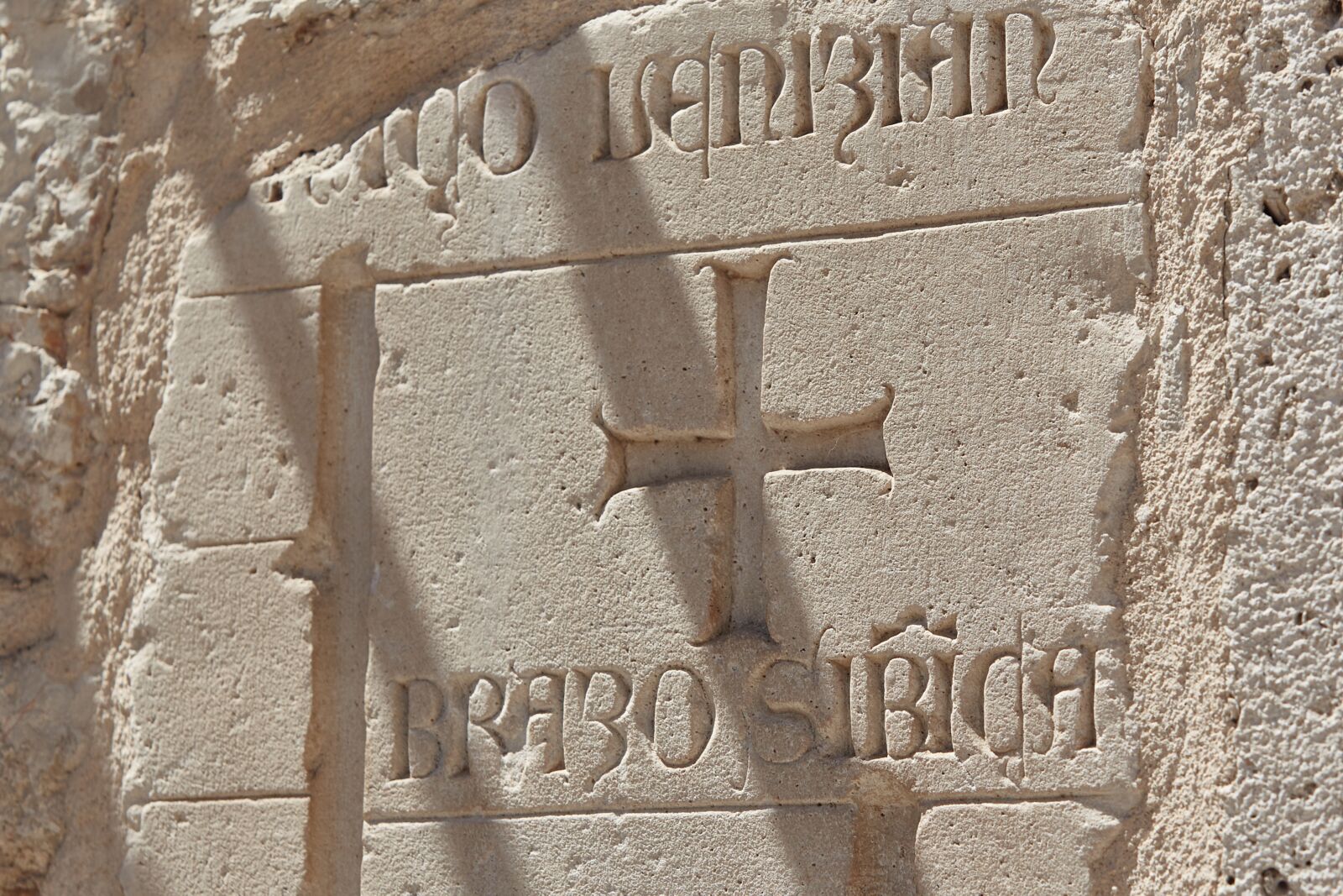 A stone wall with carved inscriptions, including a prominent 'H' and the text 'BRABO SIRACH'.