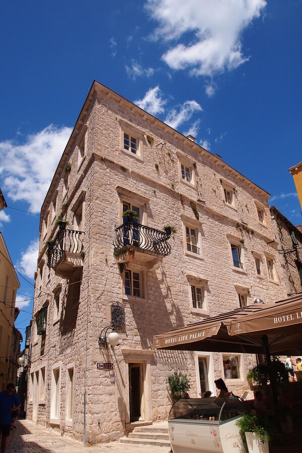 A stone building with a balcony, a sign for Hotel Life Palace, and a gelato stand.