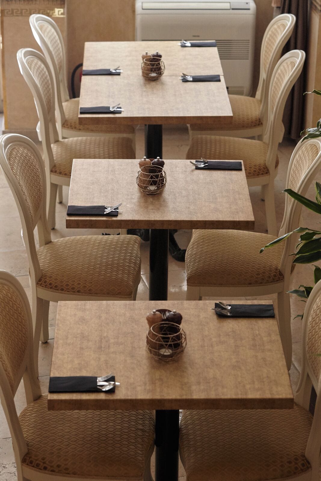 Un comedor con mesas cuadradas, sillas de mimbre y una unidad central de aire acondicionado.