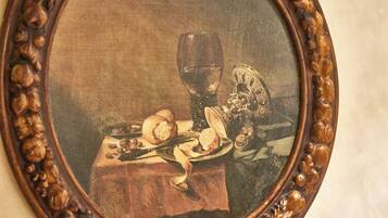 Une peinture représentant une nature morte, encadrée, avec une table, un verre de vin et divers aliments.