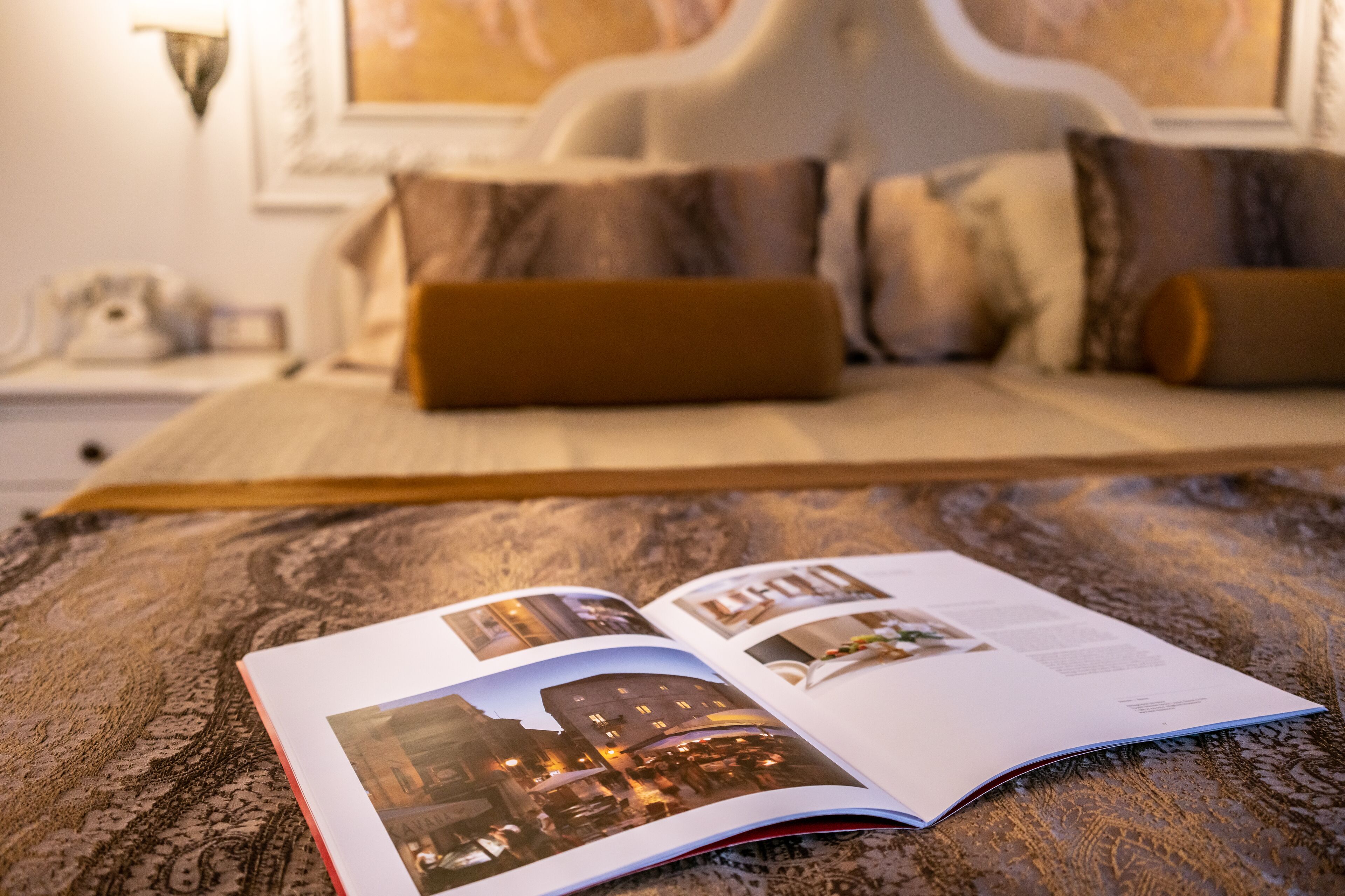 Eine offene Zeitschrift auf einem Bett mit einem gemusterten Überwurf, die Fotos von Gebäuden und Text zeigt.