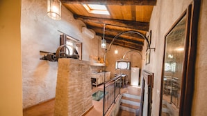 A rustic interior with a stone pillar, wooden beams, and a staircase leading to a balcony.