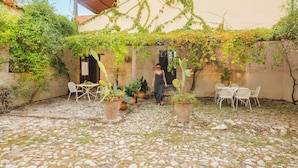 A courtyard with a stone floor, potted plants, and outdoor furniture.