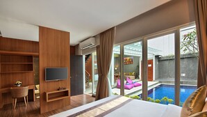 A modern hotel room with a large bed, a TV, a desk, and a view of a swimming pool. - Bellevue Heritage Villas Nusa Dua (Nusa Dua)