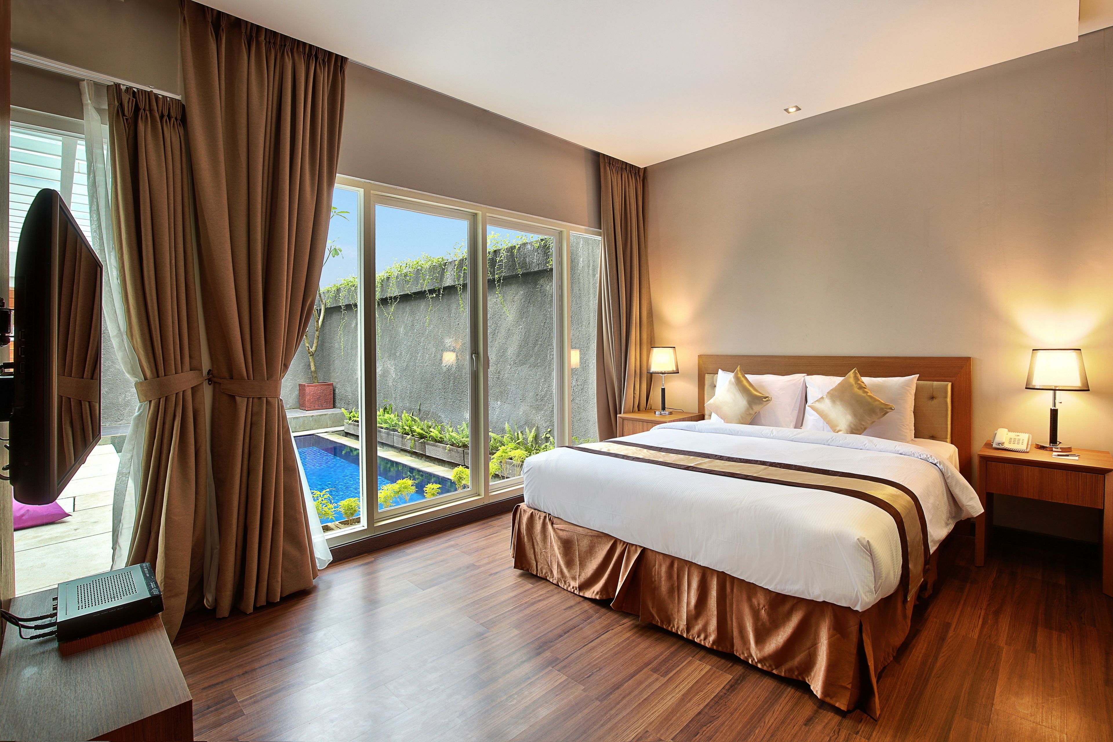 A hotel room with a large bed, two bedside tables with lamps, a TV, and a view of a swimming pool.