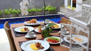 A dining table with breakfast items, a white orchid, and a view of a pool. - Bellevue Heritage Villas Nusa Dua (Nusa Dua)