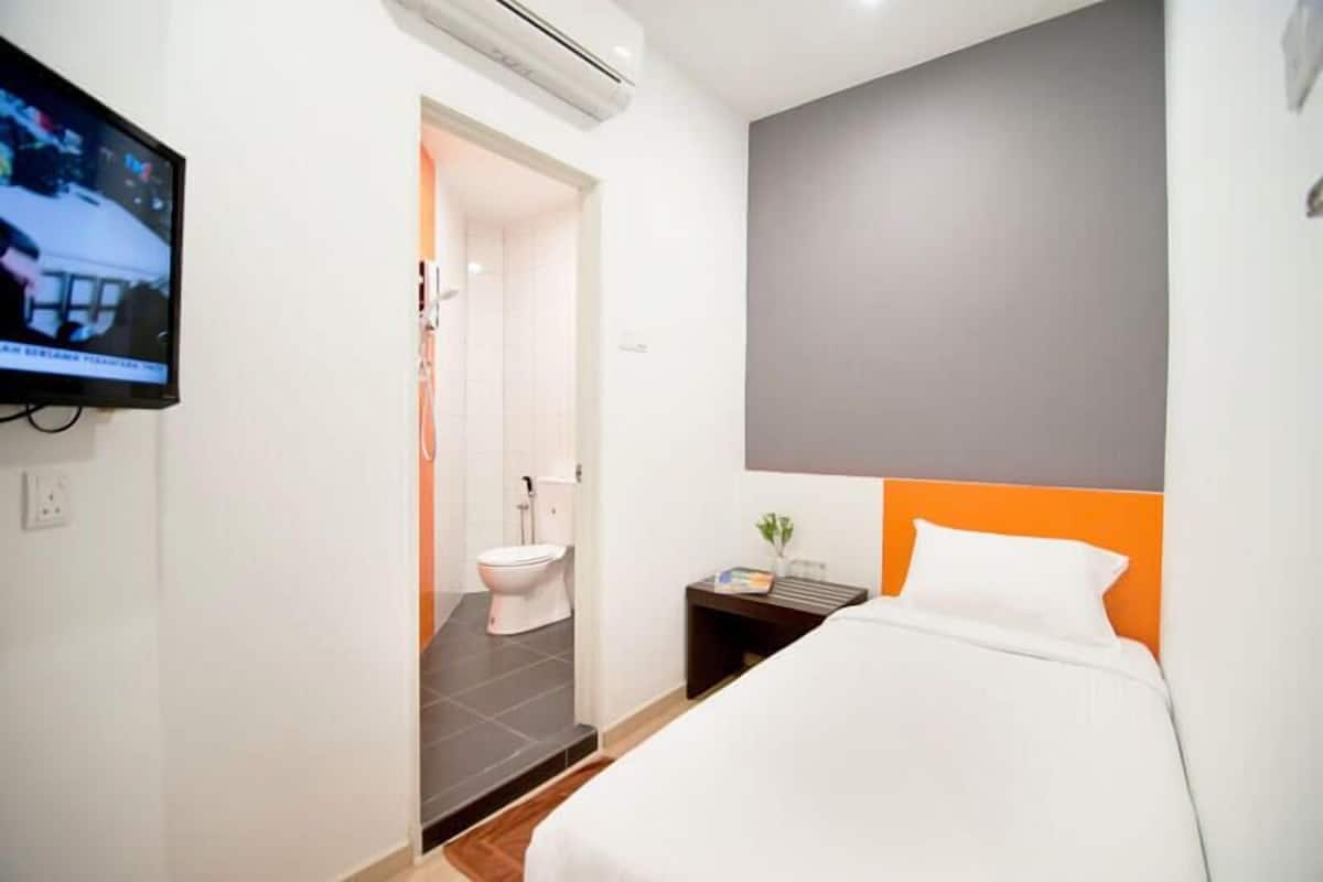 Een hotelkamer met een bed, nachtkastje, televisie en een badkamer zichtbaar door een open deur.