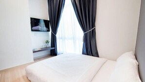 A bedroom with a bed, a TV mounted on the wall, and a window with curtains.