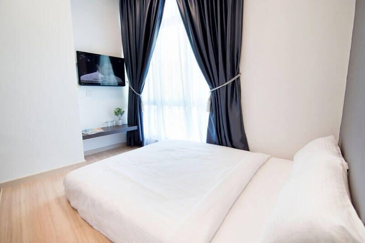 Een slaapkamer met een bed, een aan de muur bevestigde televisie en een raam met gordijnen.