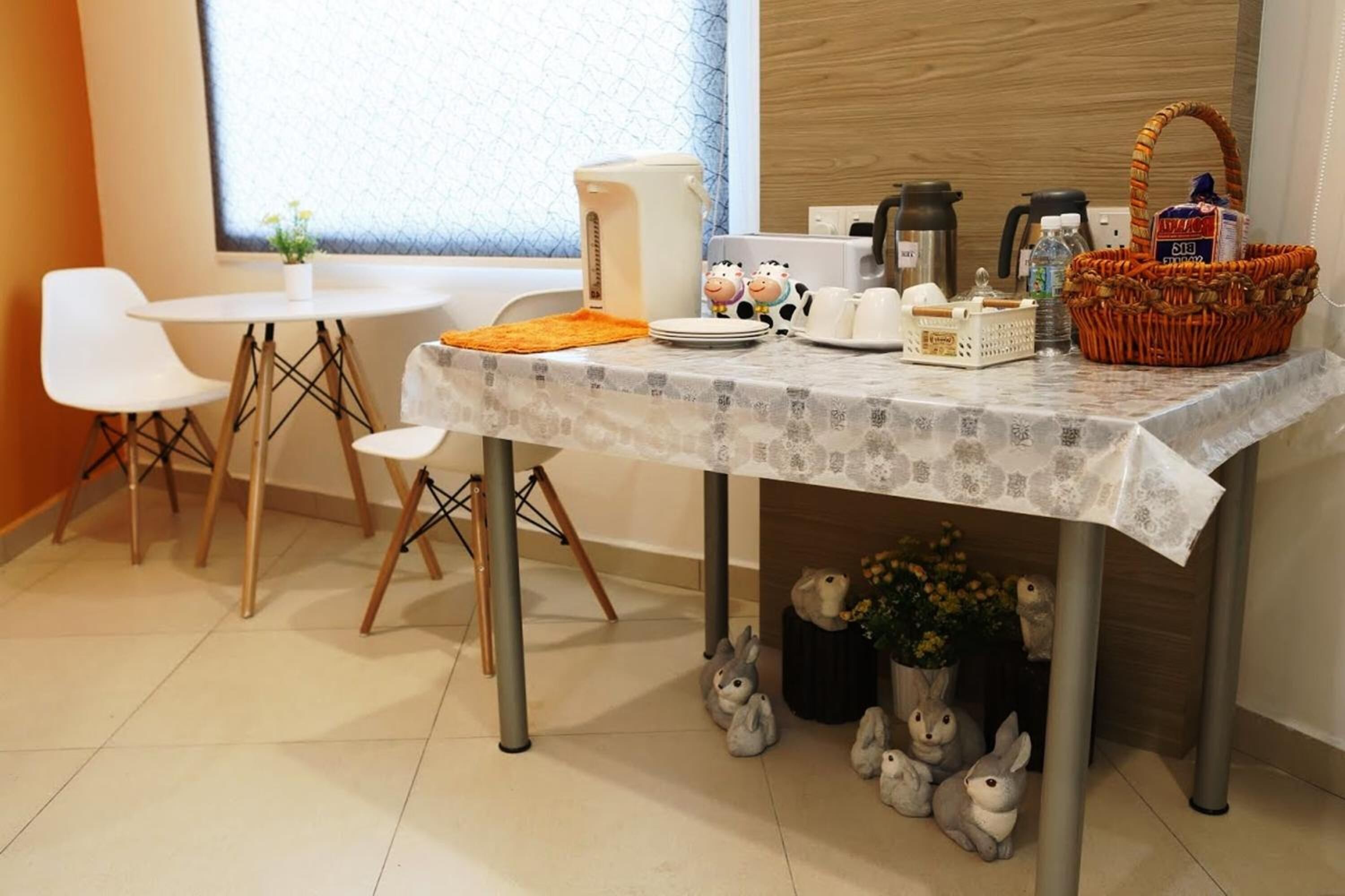 Een eethoek met een gedekte tafel voor twee personen, een koffiezetapparaat, een mand en decoratieve items, waaronder knuffeldieren.