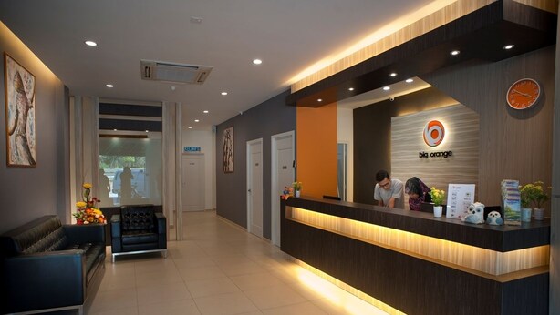 A reception area with a dark wood reception desk, a clock, and a logo for 'big orange'.