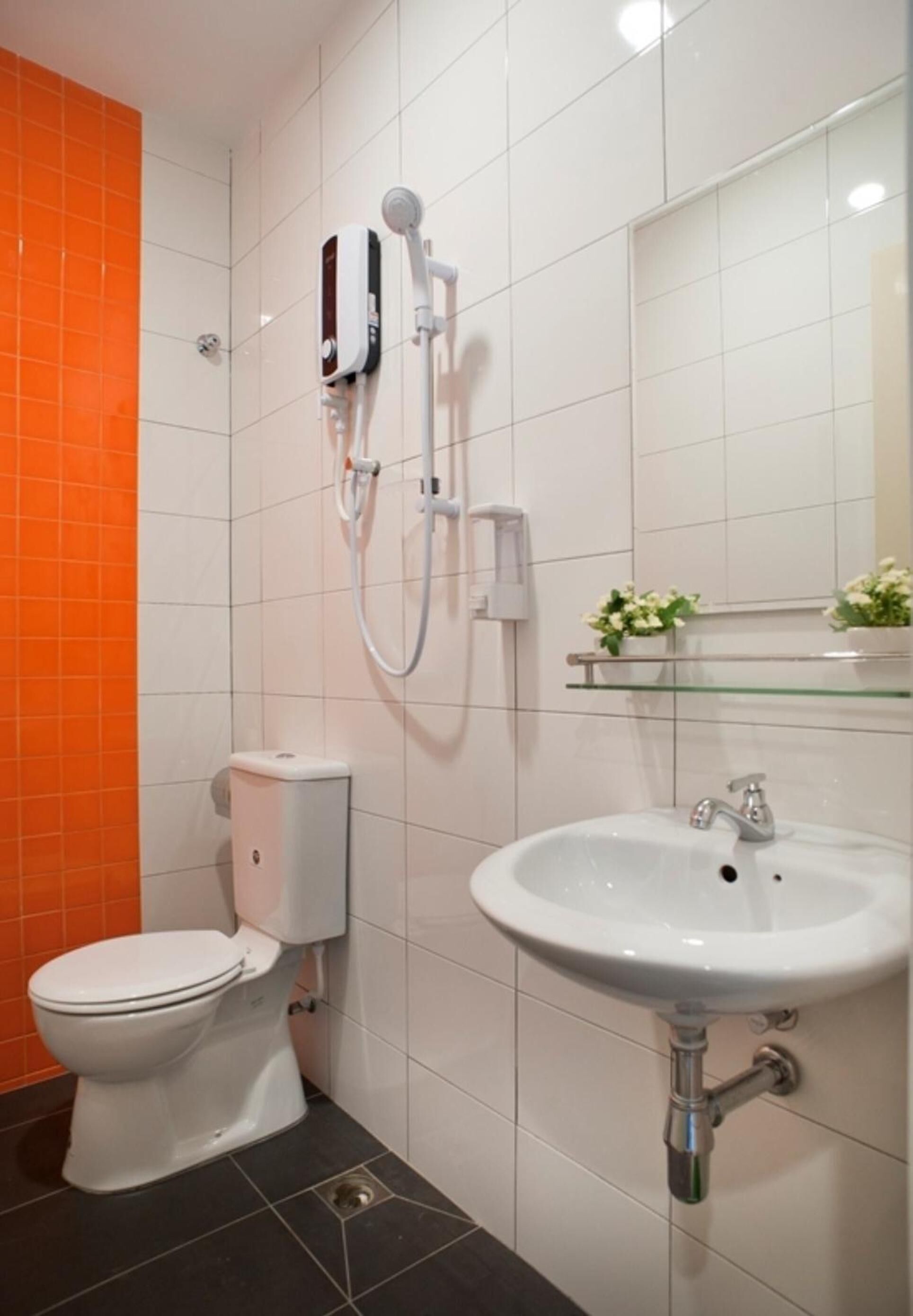 Un baño con inodoro, bidé, lavabo y repisa de vidrio con flores.