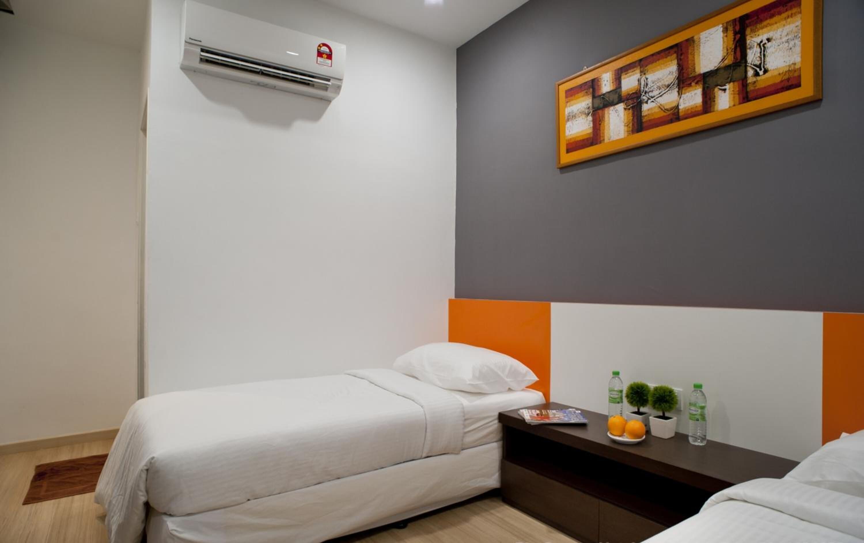 A hotel room with two single beds, a small table with a magazine, two potted plants, and an air conditioning unit on the wall.