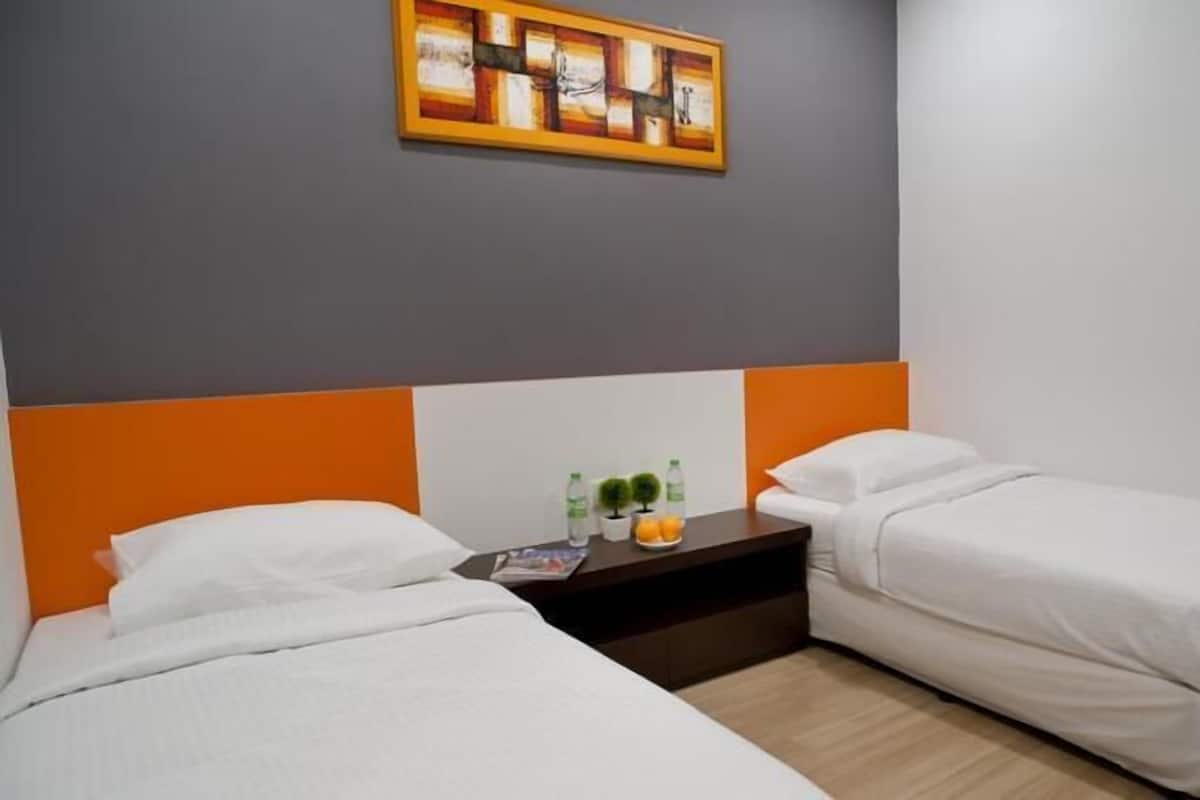 Een hotelkamer met twee enkele bedden, een nachtkastje met een fles water en fruit, en een schilderij aan de muur.