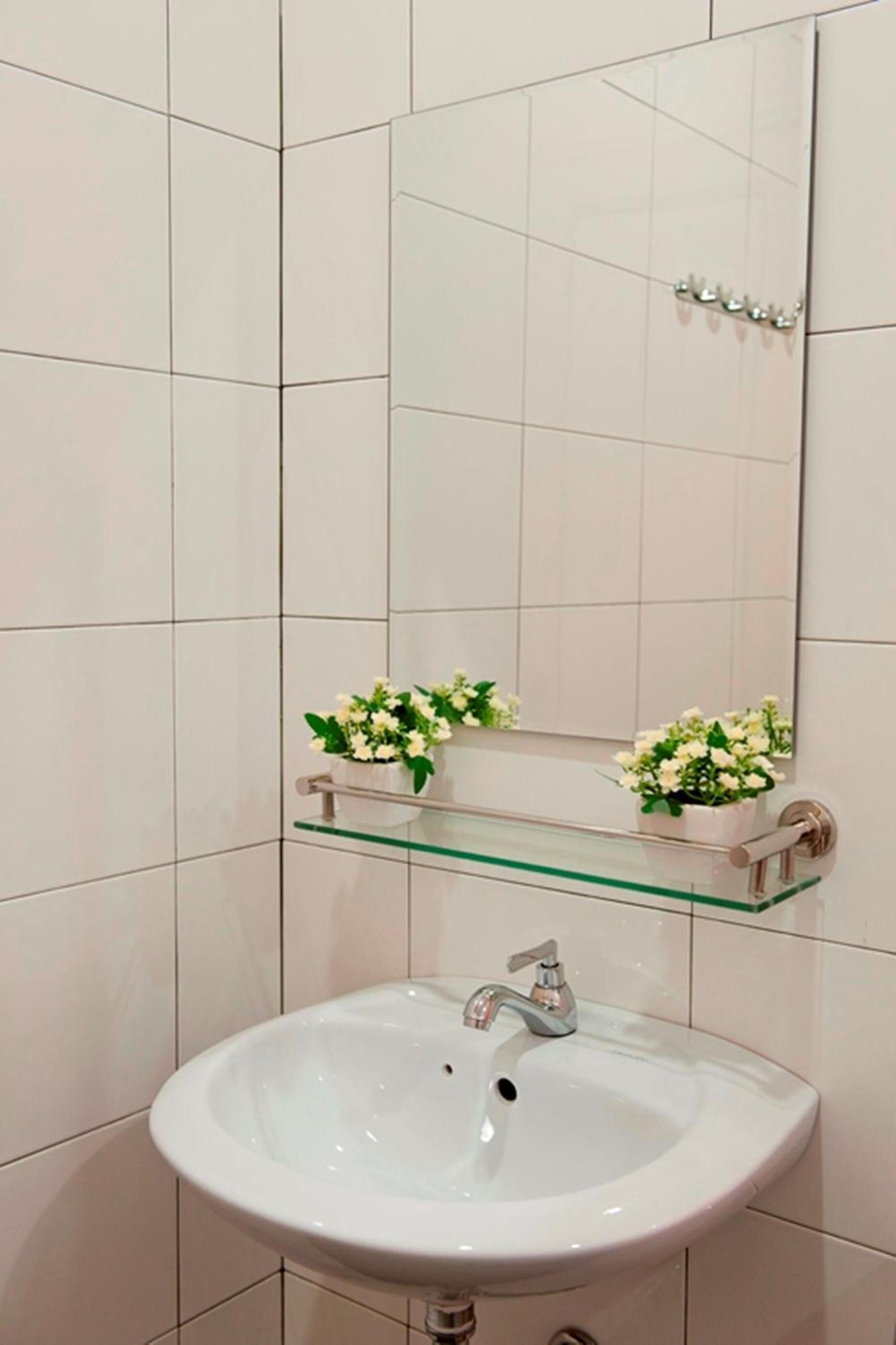A bathroom with a white sink, a mirror, and two flower arrangements on a shelf.